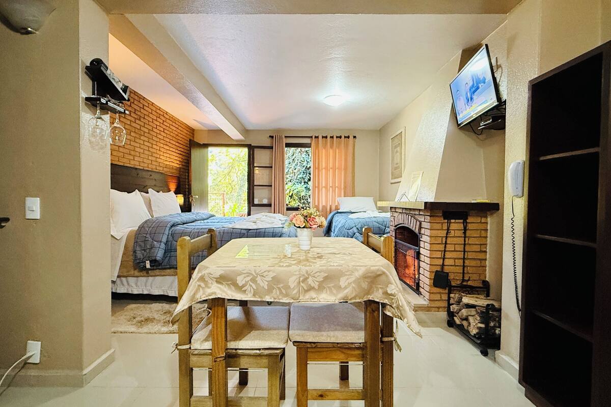 Una habitación pequeña con dos camas, una mesita, un televisor y una chimenea.