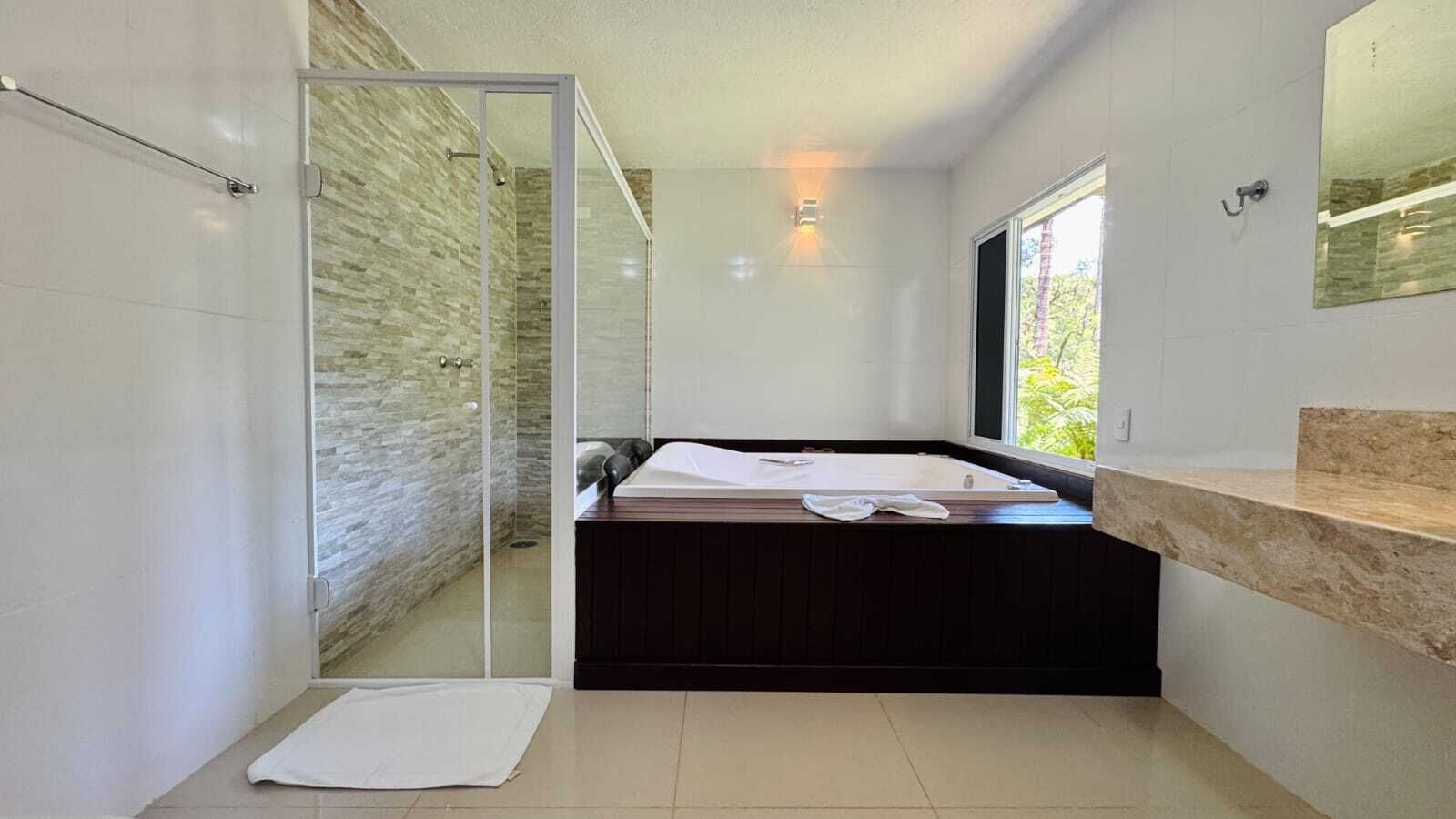 A modern bathroom with a glass shower enclosure, a built-in bench, and a large window providing natural light.