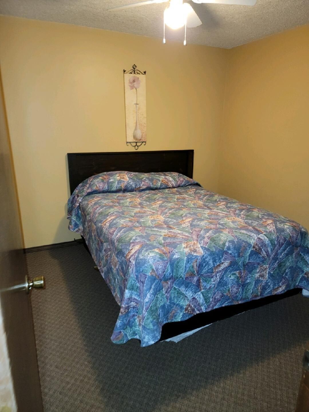 A single bed with a patterned bedspread in a room with beige walls and a dark headboard.