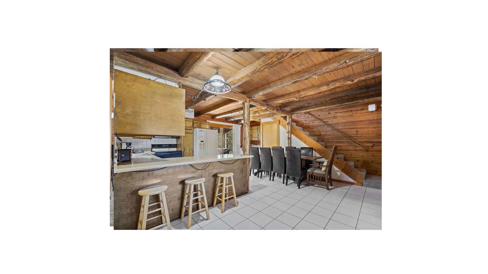 A rustic kitchen with a wooden ceiling, a bar area with stools, and a staircase.