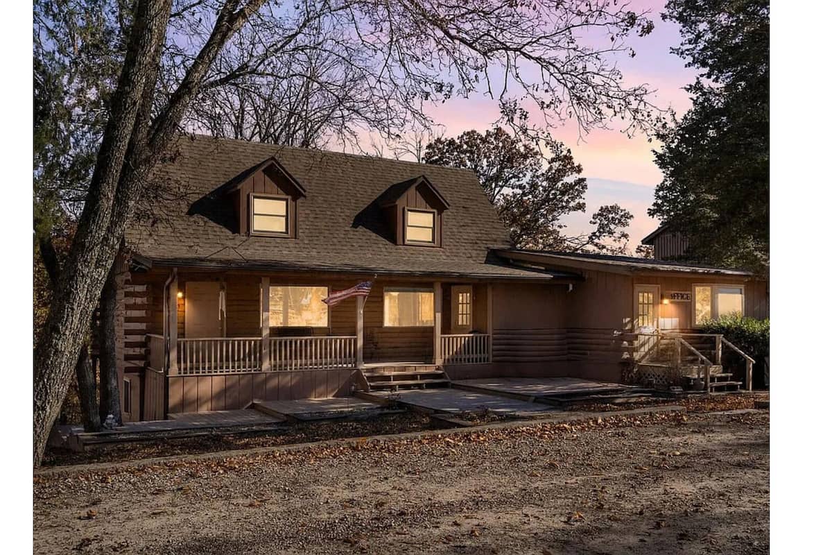 A two-story log cabin with a porch, a flag, and a small office.