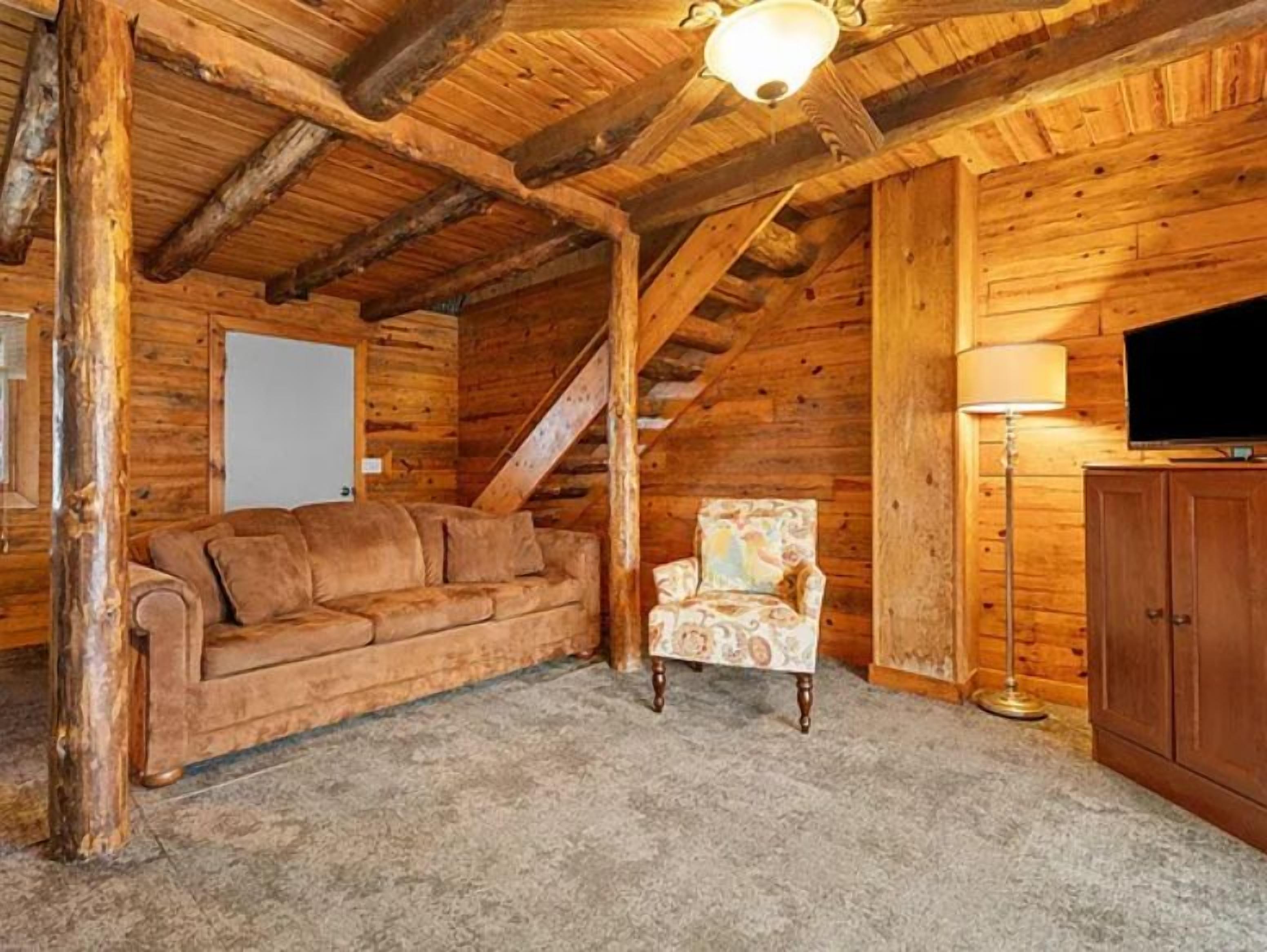 A log cabin interior with a sofa, armchair, and wooden cabinet.