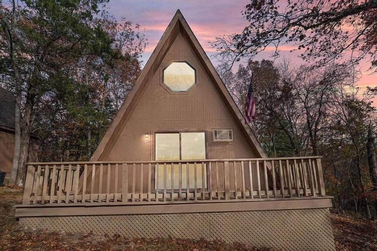 A triangular wooden cabin with a large octagonal window, a balcony with a railing, and a door.