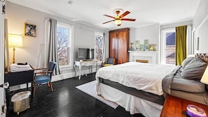 Ein Hotelzimmer mit Bett, Schreibtisch, Stuhl, Fernseher und Deckenventilator.