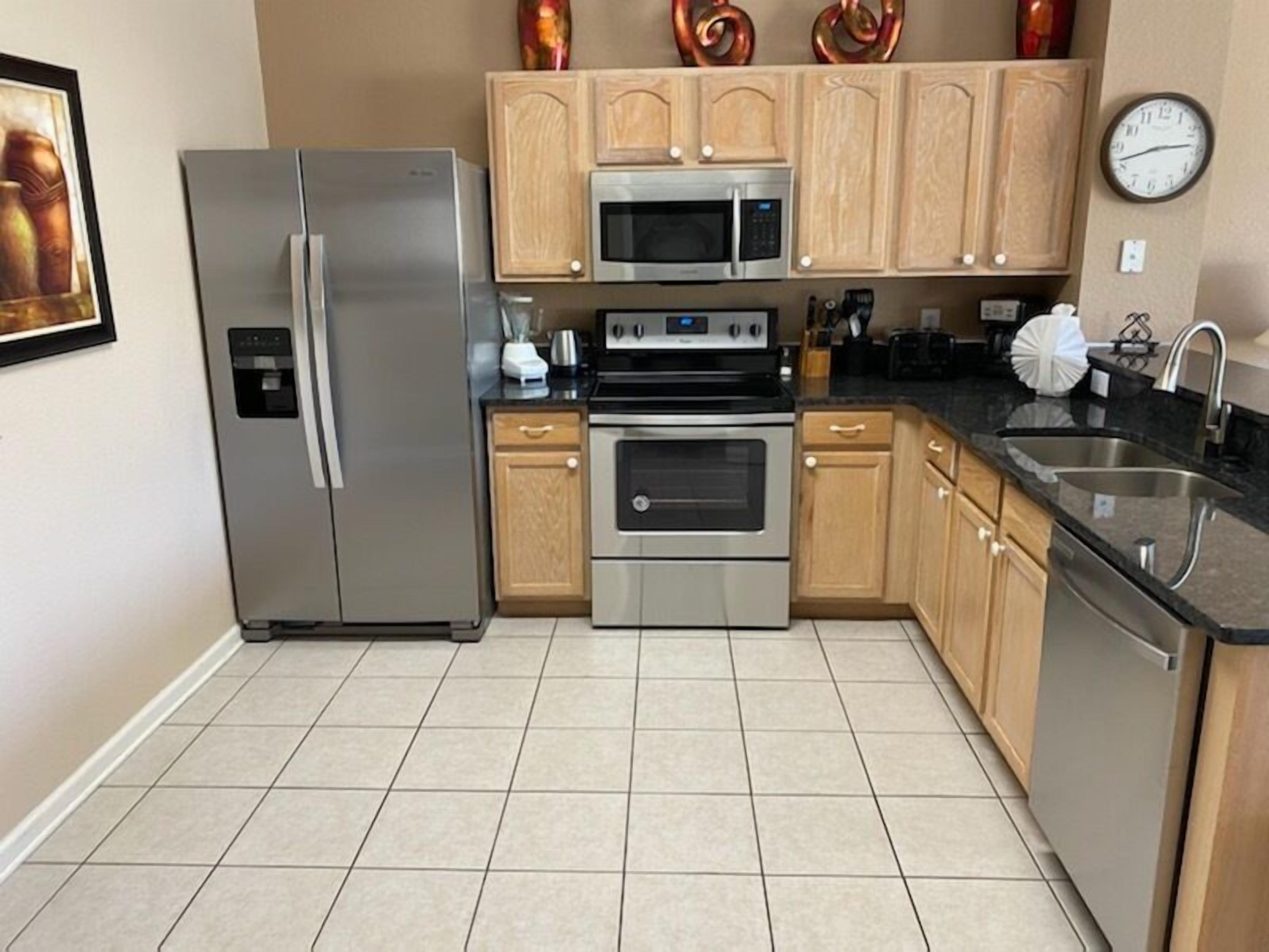 A modern kitchen with stainless steel appliances, wooden cabinets, and a tiled floor.