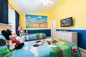 A child's room with Mickey Mouse plush toys, a bed with a Mickey Mouse-themed bedspread, a wall mural of a carnival, and a television on the wall. - Three BR * 2 Miles to Disney, pool, free WiFi and more (Kissimmee)