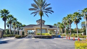 A gated entrance with a palm tree, a covered pavilion, and a clear blue sky. - Three BR * 2 Miles to Disney, pool, free WiFi and more (Kissimmee)
