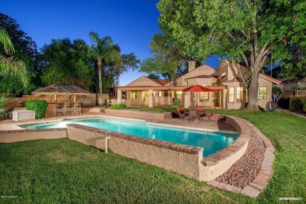 A residential property with a swimming pool, outdoor seating, and a covered patio area.