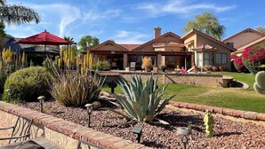 A residential property with a patio area, a red umbrella, and a well-maintained garden with cacti and other plants. - Waterfront, LuxuryVilla with Private Pool- (Chandler)