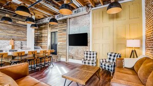 A spacious room with a wooden ceiling, a large TV mounted on the wall, and a seating area with leather sofas and chairs. - Downtown+FREE Parking+Walk Everywhere+Forsyth Park (Savannah)