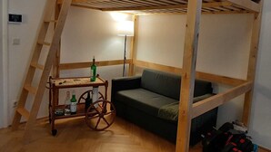 Kerrossängyllä varustettu huone, jossa on puinen tikapuu, pieni pöytä pulloineen, vihreä sohva ja lamppu.