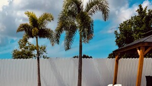 A clear blue pool with lounge chairs, palm trees, and a white fence. - Ila's Beach House: Near IMG-Heated Salt Pool- Pets OK-Modern Organic Smart Home (Bradenton)