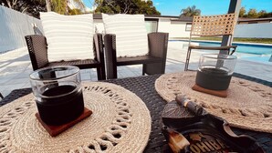 A patio with wicker furniture, a glass of dark beverage, and a bag of snacks. - Ila's Beach House: Near IMG-Heated Salt Pool- Pets OK-Modern Organic Smart Home (Bradenton)