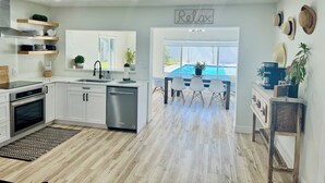 A modern kitchen with white cabinets, a dishwasher, and a dining area with a pool view. - Ila's Beach House: Near IMG-Heated Salt Pool- Pets OK-Modern Organic Smart Home (Bradenton)