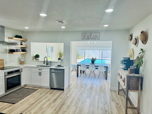 A modern kitchen with white cabinets, a dishwasher, and a dining area with a pool view.
