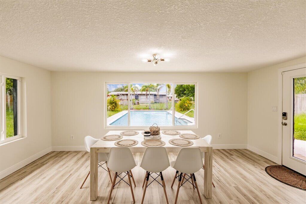 Zona pranzo con vista su una piscina, un tavolo bianco con quattro sedie e una ventola a soffitto.