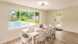 A dining area with a table set for six, large windows, and a view of a backyard with a pool. - Ila's Beach House: Near IMG-Heated Salt Pool- Pets OK-Modern Organic Smart Home (Bradenton)