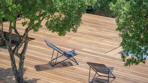 Une terrasse en bois avec deux chaises longues et un arbre.