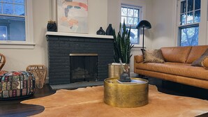 A living room with a fireplace, leather sofa, patterned ottoman, and a large rug. - Chic Bungalow Located In The Heart Of Wichita (Wichita)