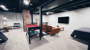 Une pièce avec une table de billard, un canapé en cuir, un téléviseur fixé au mur et un mur décoratif en briques.