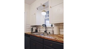 A kitchen with white cabinets, a wooden countertop, a black faucet, and a pendant light. - Chic Bungalow Located In The Heart Of Wichita (Wichita)