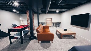 A room with a pool table, a leather sofa, a coffee table, a TV, and a brick column. - Chic Bungalow Located In The Heart Of Wichita (Wichita)