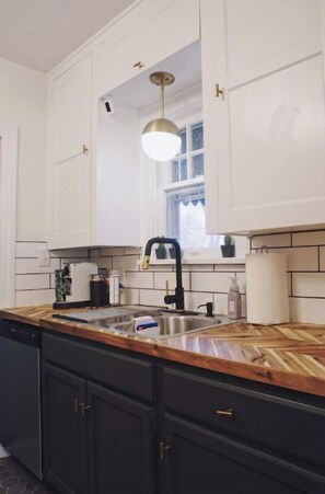 A kitchen with white cabinets, a wooden countertop, a black faucet, and a pendant light. - Chic Bungalow Located In The Heart Of Wichita (Wichita)