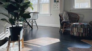 A spacious room with a large potted plant, a wicker chair, a quilted ottoman, and a dining table. - Chic Bungalow Located In The Heart Of Wichita (Wichita)
