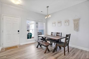 Un comedor con una mesa y sillas de madera, una puerta blanca y una pared con letras enmarcadas.
