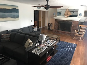 A living room with a dark-colored sofa, a coffee table with magazines, a fireplace, and a rocking chair.