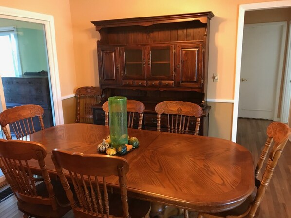 Una mesa de comedor con cuatro sillas, un jarrón verde y un aparador de madera al fondo.