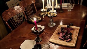 A wooden dining table set for a meal with candles, plates, cutlery, and a serving of meat. - SUMMER IN THE POCCONOS ! (Tafton)