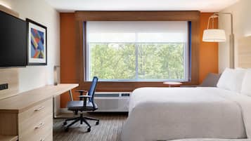 A hotel room with a bed, a desk, a chair, a TV, and a window with a view of trees.