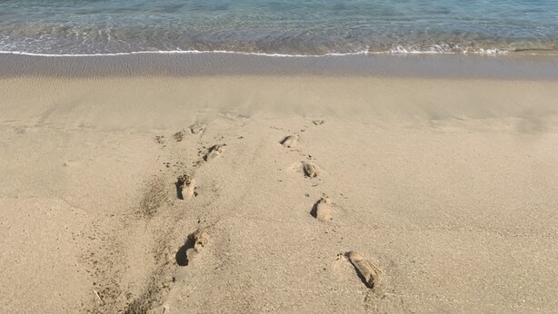 Une plage où l’on peut voir des empreintes de pas dans le sable, sous un ciel bleu et dégagé.
