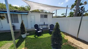 Un espace patio aménagé avec une table et des chaises, entouré de plantes en pot et d’une clôture blanche.