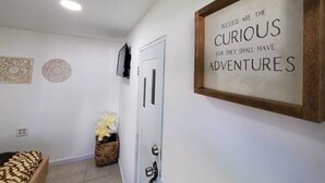 Un couloir orné d’une citation inspirante encadrée, une porte, un petit lit et des éléments décoratifs sur les murs.