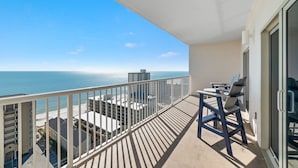 Un balcon avec vue sur l’océan, une table avec des chaises et une porte-fenêtre coulissante.