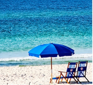 Een strandscène met een blauwe parasol en twee strandstoelen.