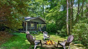 A covered outdoor seating area with two Adirondack chairs and a fire pit.
