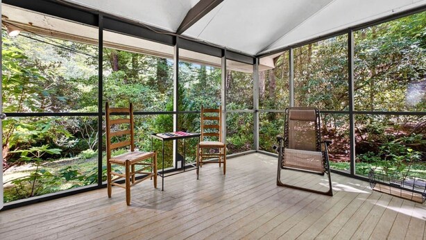 A room with large windows, wooden flooring, and two wooden chairs.