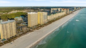 A coastal cityscape with high-rise hotels along a sandy beach, a clear sky, and a view of the ocean.