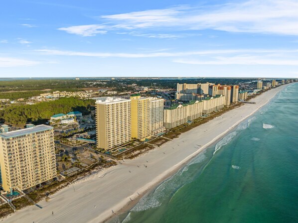 A coastal cityscape with high-rise hotels along a sandy beach, a clear sky, and a view of the ocean.