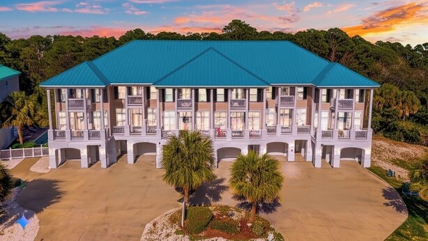 A multi-story hotel with a blue roof, multiple balconies, and a landscaped front yard with trees.