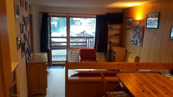 A cozy room with a wooden bench, a red chair, a table, and a television on the wall.