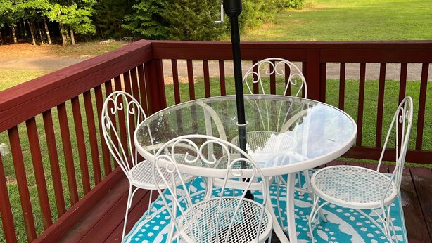Un patio con una mesa redonda y sillas blancas, una sombrilla color beige y un tapete azul estampado.