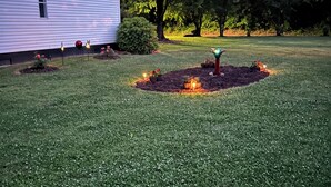Un césped cuidado con un pequeño jardín decorado con luces y un árbol en el centro.