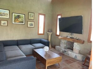A living room with a sectional sofa, a flat-screen TV mounted above a stone fireplace, and several framed pictures on the wall.