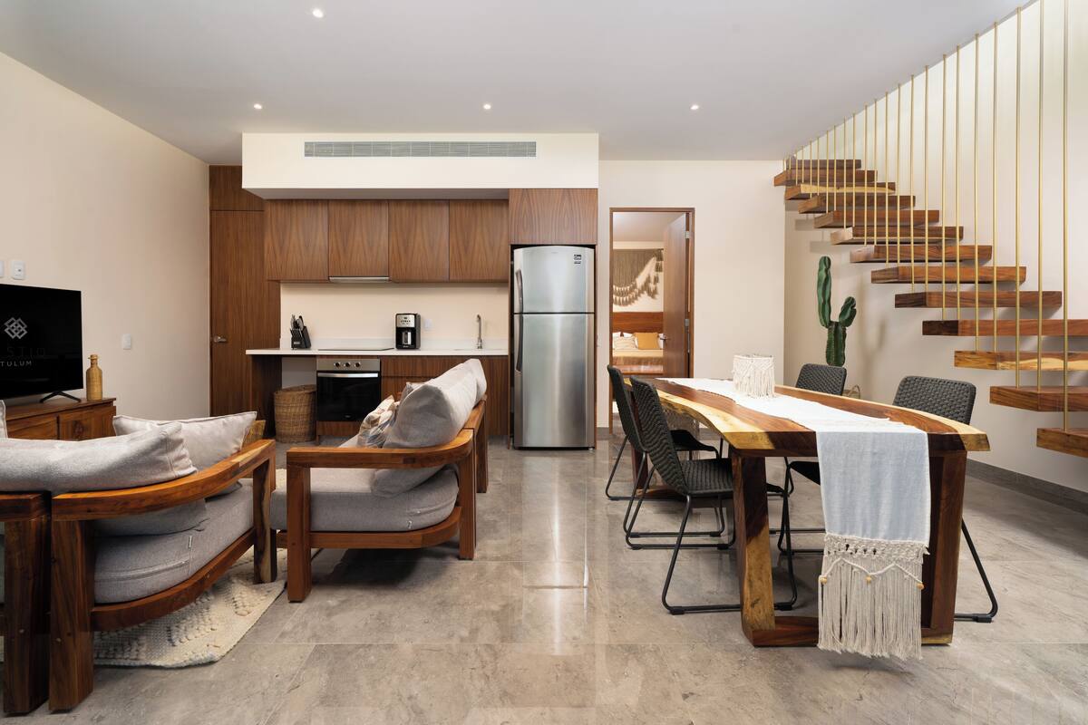 A modern kitchen with wooden cabinets, a stainless steel refrigerator, and a dining area with a wooden table and chairs.