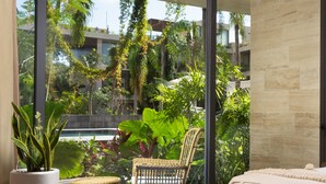 A modern bedroom with a large sliding glass door leading to a balcony with lush greenery and a pool view. - Mistiq Tulum (Tulum)