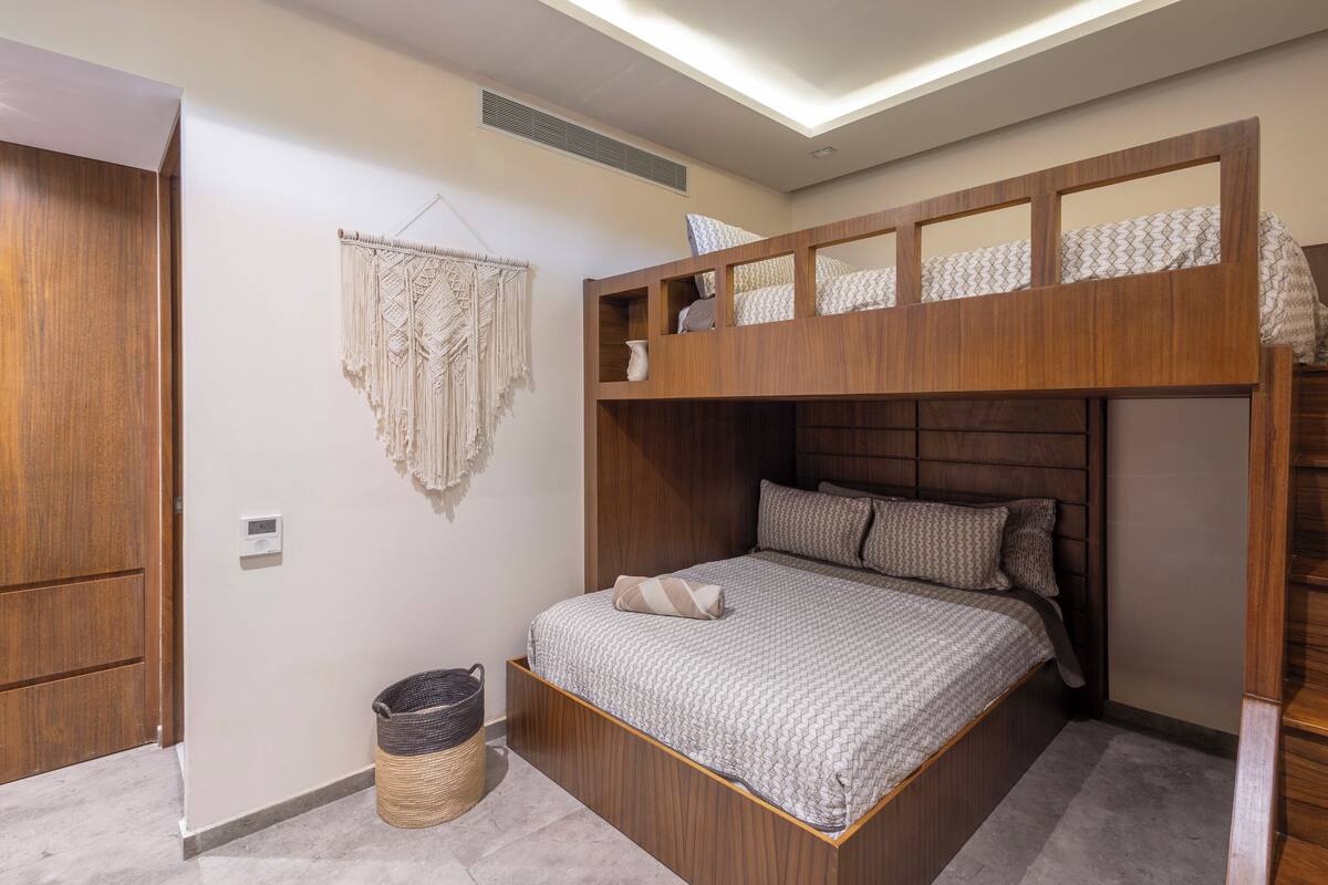 A bunk bed with a wooden headboard, a macrame wall hanging, and a small basket on the floor.